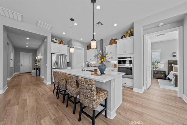 kitchen featuring light countertops, stainless steel appliances, a center island with sink, and white cabinets