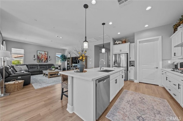 kitchen with light countertops, appliances with stainless steel finishes, a center island with sink, and white cabinets