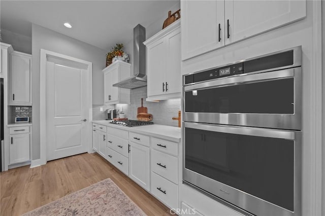 kitchen with stainless steel appliances, light countertops, wall chimney range hood, and white cabinetry