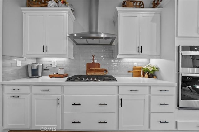 kitchen with appliances with stainless steel finishes, light countertops, white cabinetry, and wall chimney exhaust hood