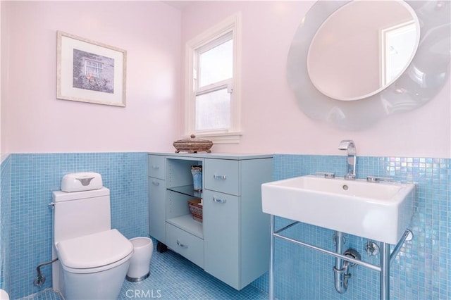 half bathroom with tile walls, toilet, wainscoting, a sink, and tile patterned flooring