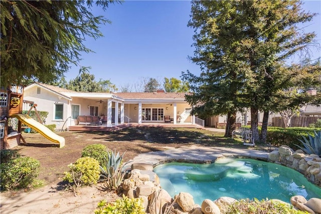 back of property with a playground, ceiling fan, and stucco siding