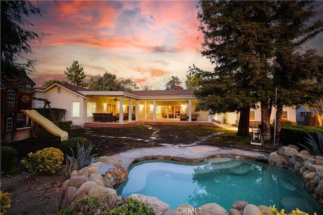 back of property at dusk featuring a playground, a patio area, and an outdoor pool