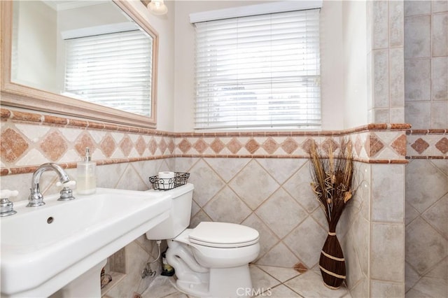 half bath featuring toilet, plenty of natural light, tile walls, and a sink