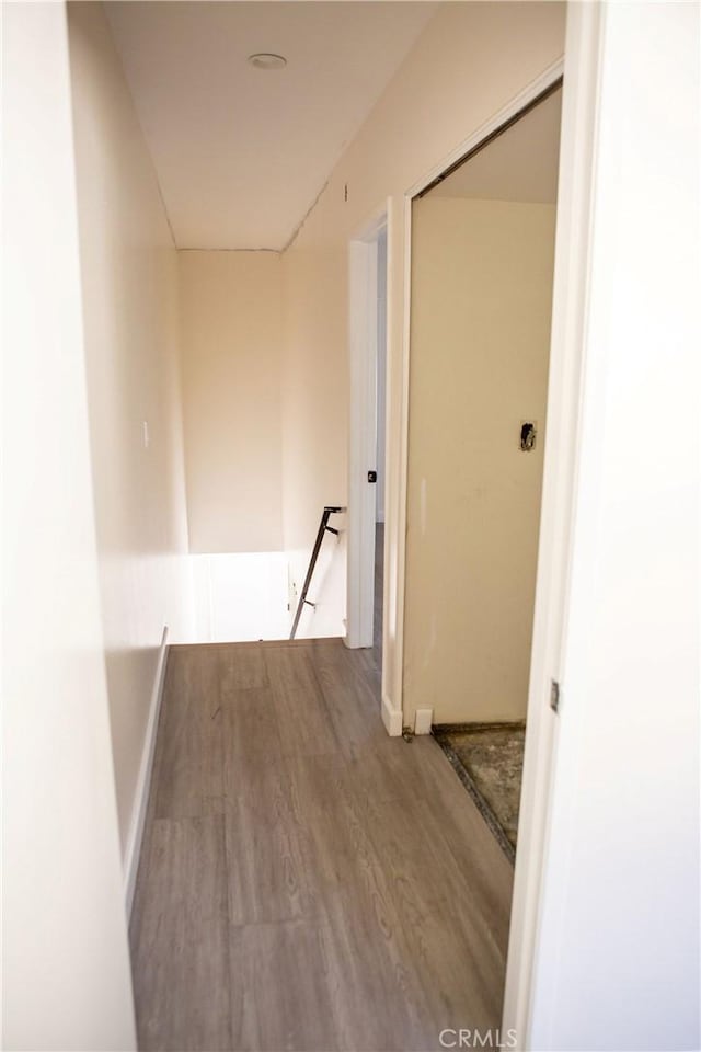 corridor with baseboards, wood finished floors, and an upstairs landing