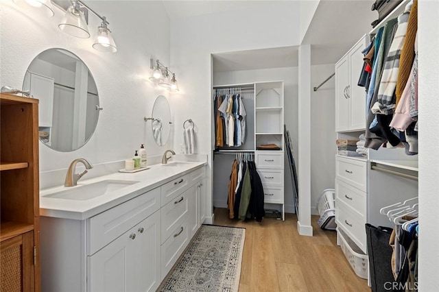 full bathroom featuring double vanity, a spacious closet, wood finished floors, and a sink