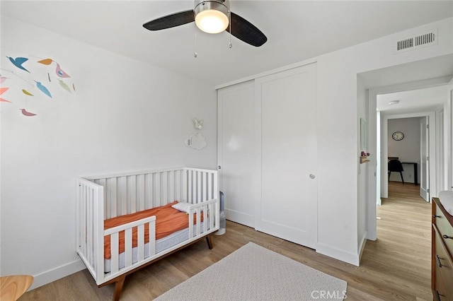 bedroom with a closet, visible vents, a ceiling fan, wood finished floors, and a crib