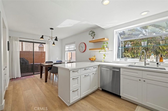 kitchen with a peninsula, a sink, light countertops, dishwasher, and light wood finished floors