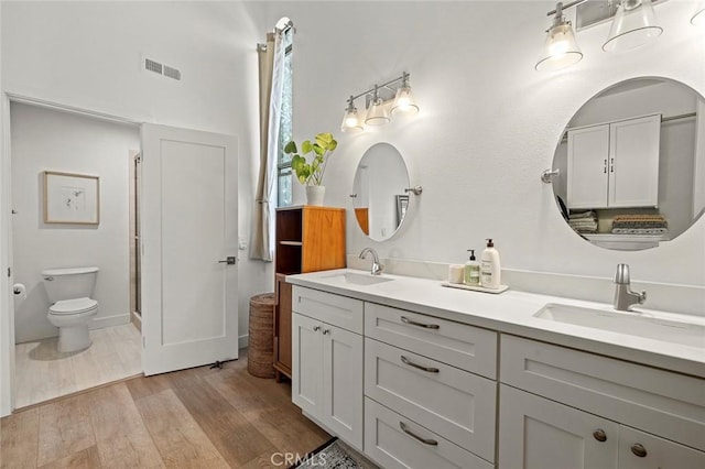 full bathroom with visible vents, a sink, toilet, and wood finished floors