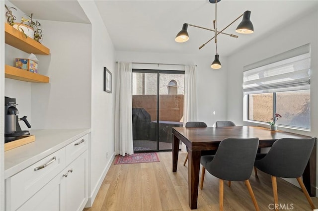 dining room featuring light wood-type flooring, a notable chandelier, plenty of natural light, and baseboards