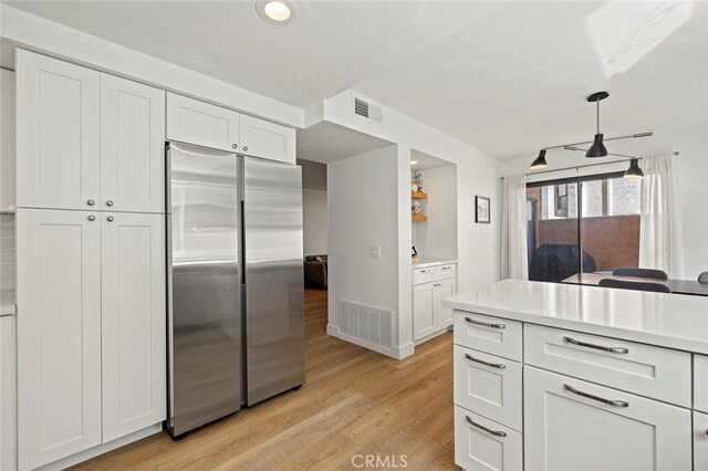 kitchen featuring light wood-type flooring, stainless steel fridge, visible vents, and white cabinets