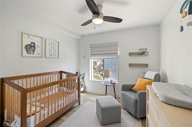 bedroom with a nursery area, wood finished floors, a ceiling fan, and baseboards