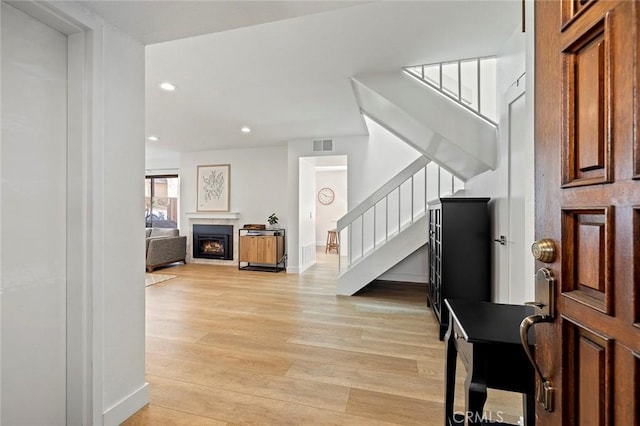 foyer featuring a warm lit fireplace, light wood-style flooring, recessed lighting, visible vents, and stairway