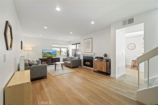 living room featuring light wood-style floors, a warm lit fireplace, visible vents, and recessed lighting