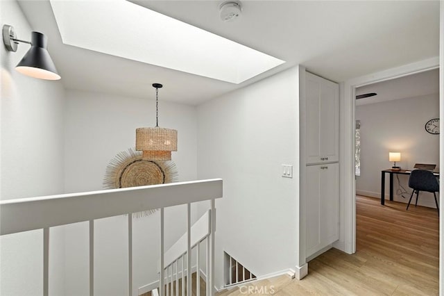 hall featuring light wood-style flooring, a skylight, an upstairs landing, and baseboards