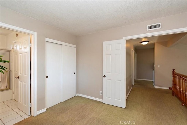 unfurnished bedroom with a closet, light colored carpet, visible vents, a textured ceiling, and baseboards