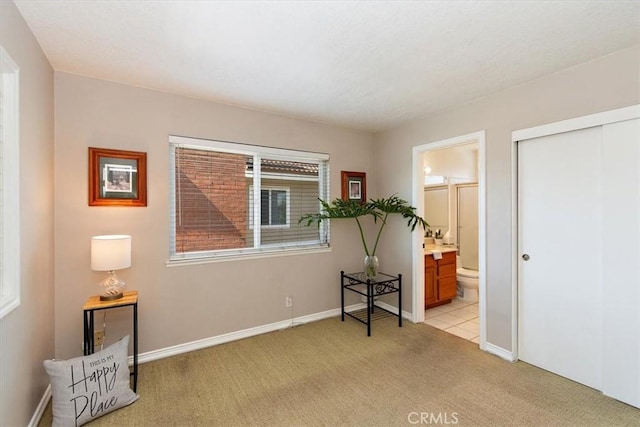 bedroom featuring light carpet, ensuite bath, baseboards, and a closet