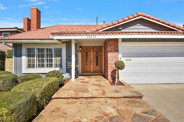 view of front of home featuring brick siding, a chimney, a garage, driveway, and a tiled roof