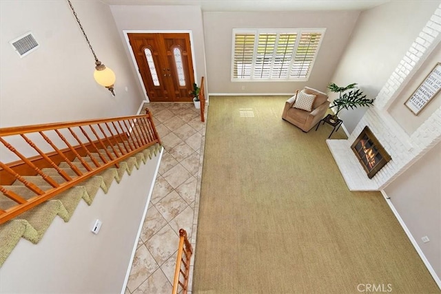 tiled entrance foyer with stairway, baseboards, a brick fireplace, and visible vents