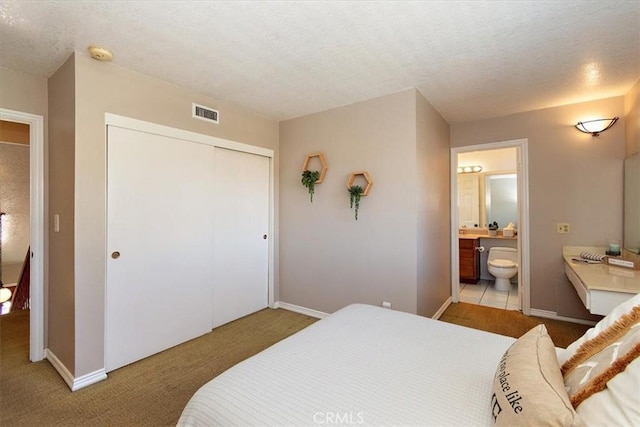 bedroom with carpet floors, a closet, visible vents, a textured ceiling, and ensuite bath