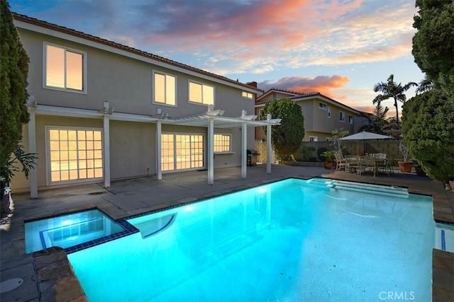 pool at dusk featuring a pool with connected hot tub, fence, a patio, and a pergola