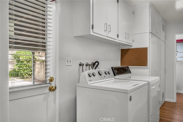 clothes washing area featuring a wealth of natural light, washing machine and dryer, cabinet space, and wood finished floors