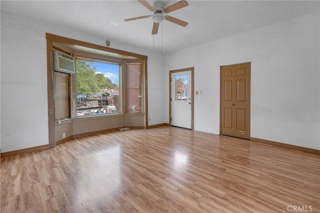 spare room featuring a wall unit AC, light wood finished floors, plenty of natural light, and ceiling fan