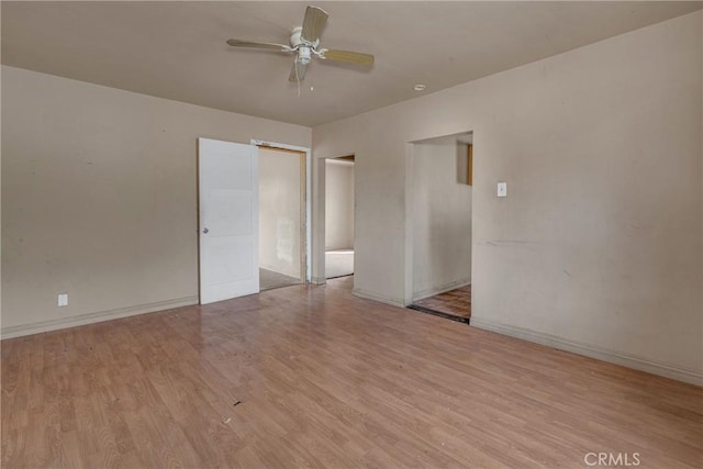 spare room with wood finished floors, a ceiling fan, and baseboards