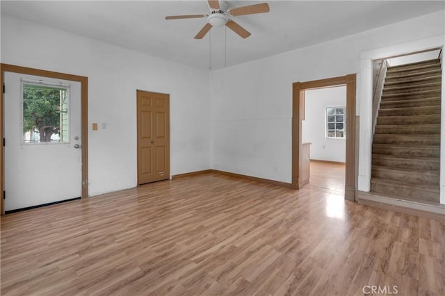 empty room with stairway, a ceiling fan, and light wood-style floors