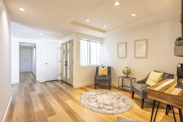 living area featuring baseboards, a tray ceiling, light wood-type flooring, and recessed lighting