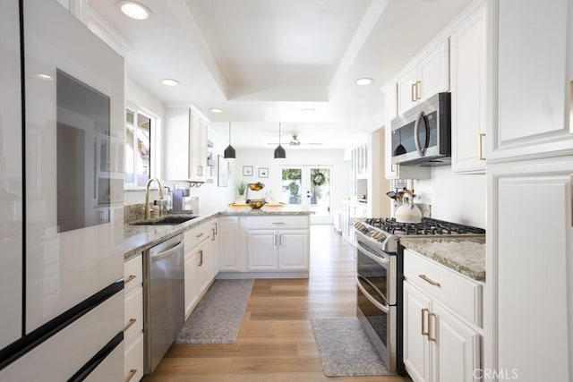 kitchen with a tray ceiling, appliances with stainless steel finishes, white cabinets, a sink, and a peninsula