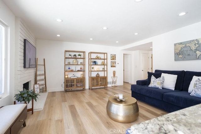 living area featuring light wood-style floors, recessed lighting, a large fireplace, and baseboards