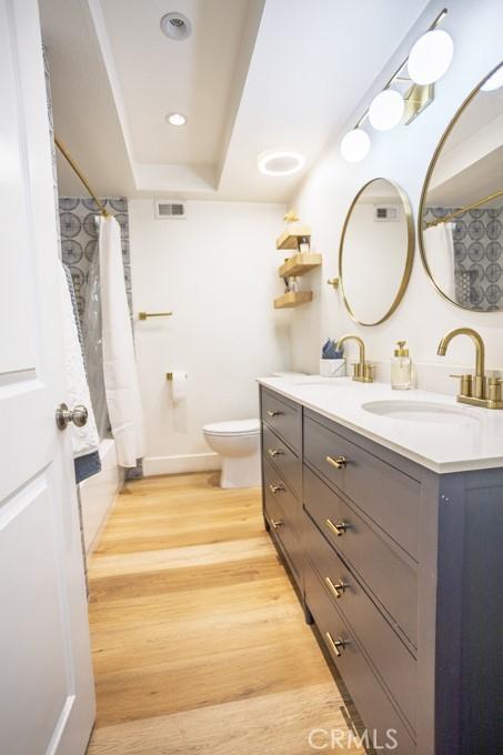 bathroom featuring toilet, wood finished floors, vanity, visible vents, and a tray ceiling