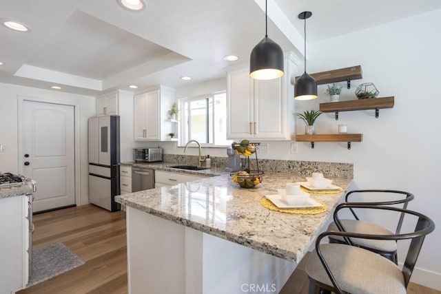 kitchen with a tray ceiling, open shelves, stainless steel appliances, a sink, and a peninsula