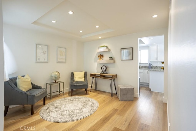 sitting room featuring a tray ceiling, light wood-style flooring, baseboards, and recessed lighting