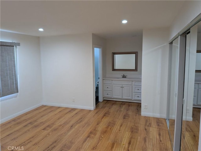 unfurnished bedroom with light wood-type flooring, baseboards, a sink, and recessed lighting