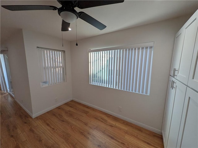 unfurnished room with wood finished floors, a ceiling fan, and baseboards