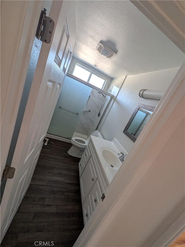 full bathroom with a textured ceiling, toilet, wood finished floors, vanity, and a shower stall