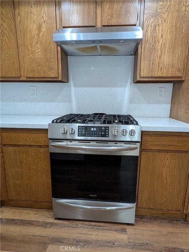 kitchen with stainless steel gas stove, brown cabinetry, wood finished floors, and under cabinet range hood