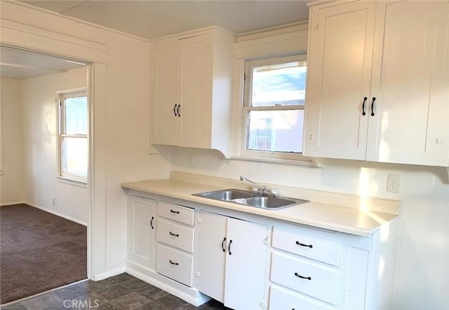 kitchen featuring dark colored carpet, light countertops, white cabinetry, a sink, and baseboards