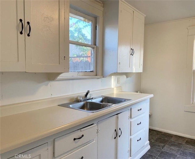 kitchen featuring white cabinets, light countertops, a sink, and baseboards