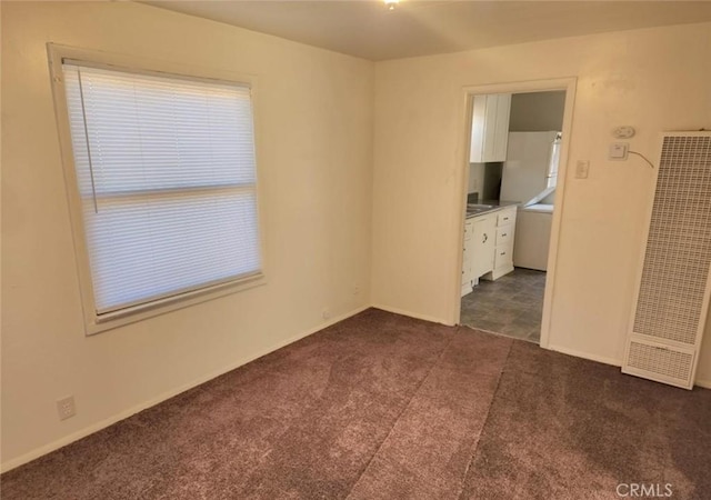 spare room with a heating unit, dark carpet, and baseboards