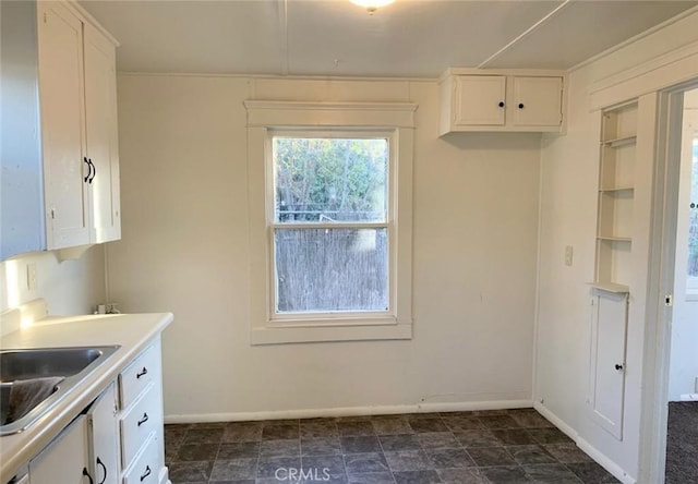 kitchen featuring light countertops, white cabinets, a sink, and baseboards