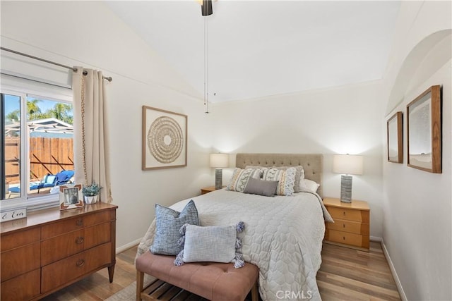 bedroom with a ceiling fan, vaulted ceiling, light wood-style flooring, and baseboards