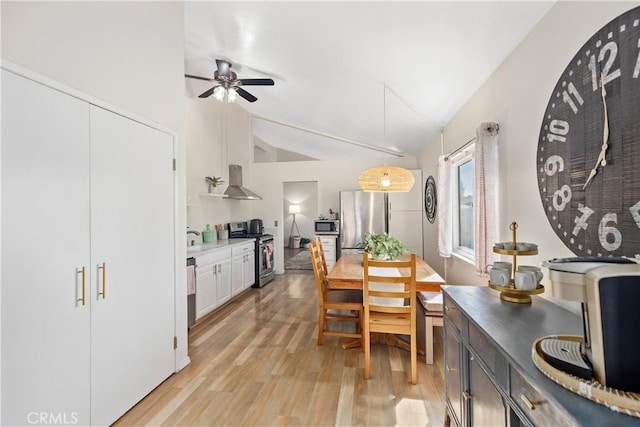 kitchen featuring light wood finished floors, wall chimney exhaust hood, appliances with stainless steel finishes, hanging light fixtures, and white cabinetry