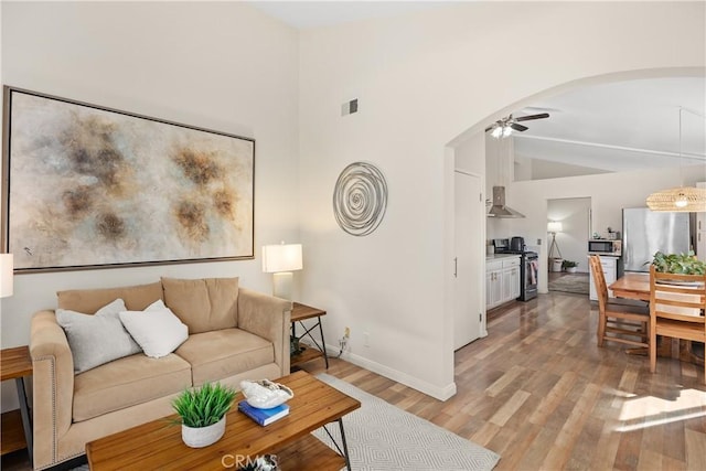 living area with arched walkways, ceiling fan, lofted ceiling, visible vents, and light wood-style floors