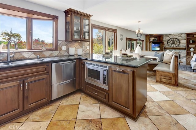 kitchen featuring backsplash, appliances with stainless steel finishes, glass insert cabinets, a sink, and a peninsula