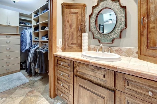 bathroom featuring a spacious closet, stone finish floor, and vanity