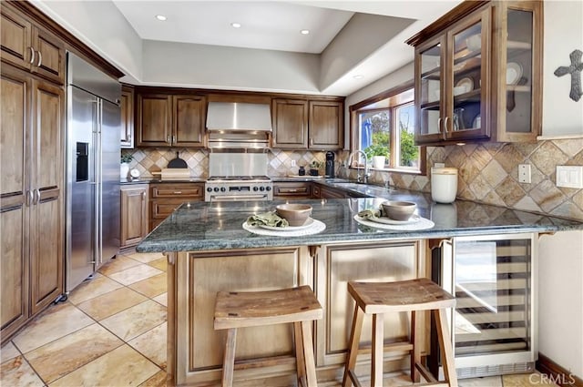 kitchen featuring wine cooler, a sink, wall chimney range hood, high quality appliances, and a peninsula