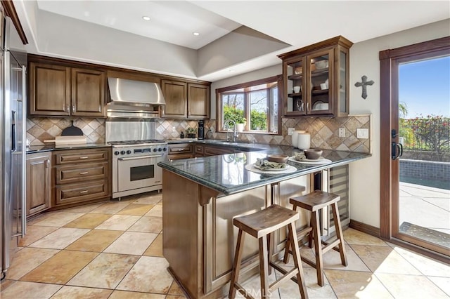 kitchen with a peninsula, a sink, high quality appliances, a kitchen breakfast bar, and wall chimney exhaust hood